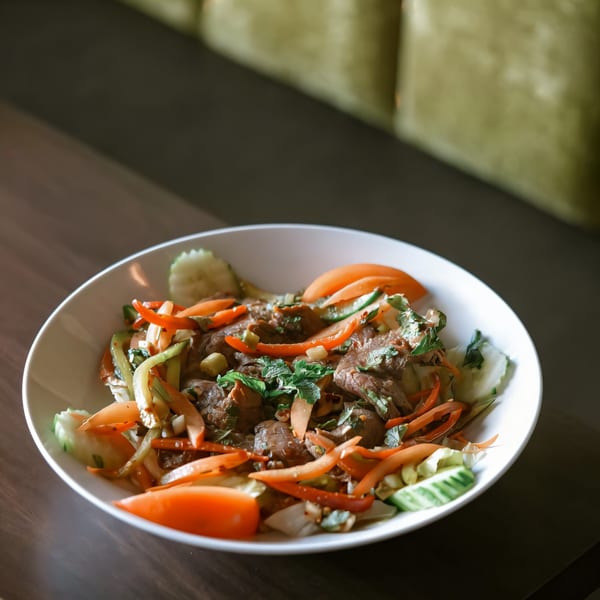 Paul's Fusion Kitchen's Asian-fusion beef salad with vegetables, herbs, and sliced tomatoes in a white bowl.