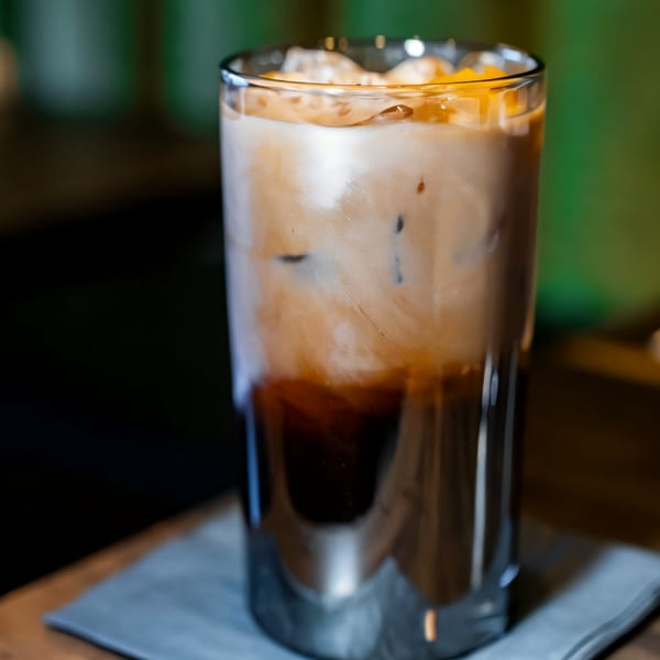 Iced coffee with milk and a dark base, topped with ice and small orange pieces.