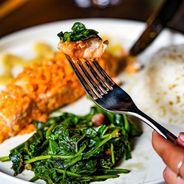A fork lifts a piece of salmon with spinach from a plate of Paul's Fusion Kitchen's salmon, rice, and greens.