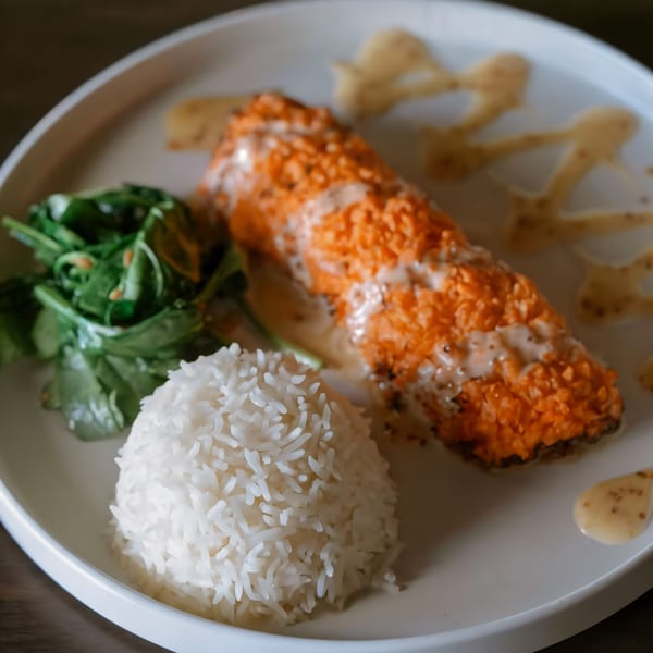 Paul's Fusion Kitchen's salmon with crispy topping, rice, and greens on a white plate.