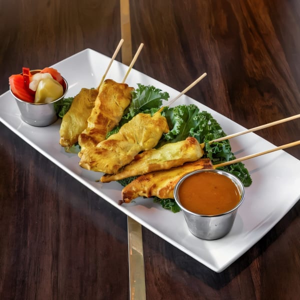 Paul's Fusion Kitchen's chicken satay skewers with peanut sauce and pickled vegetables on a white plate.